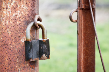 The old padlock hangs on a column of an iron fencing.