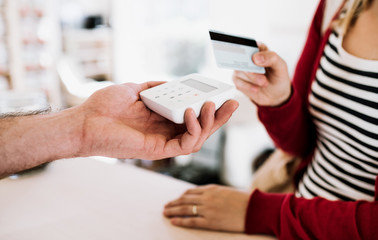 Customer and shop assistant making contactless payment using credit card in a shop.