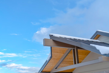 Snow covered roof against blue sky with clouds