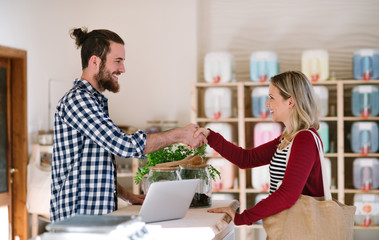 Young shop assistant and an attractive woman in a zero waste shop, shaking hands.