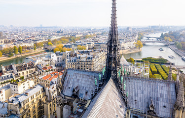 View from the tower of Notre-Dame de Paris over the ile de la Cite and the Seine with the rooftop and spire of the cathedral in the foreground and tour boats cruising on the river by a misty morning.