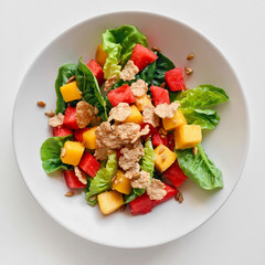 Colorful summer salad with green cos lettuce, mango, watermelon, cereal and sunflower seed on a white background, top view close up