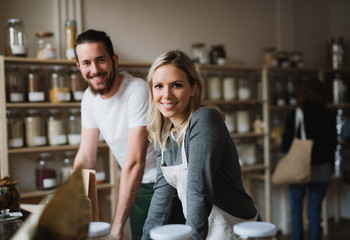 A portrait of two shop assistants standing in zero waste shop, looking at camera.