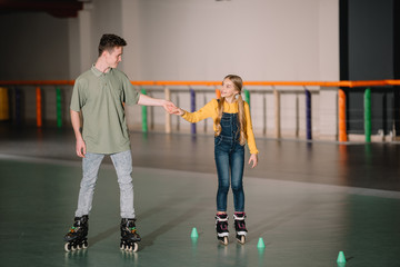 Handsome young instructor holding children hand while explaining skating technics