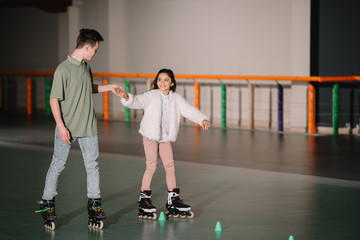 Handsome instructor holding training child on roller skates with holding hand