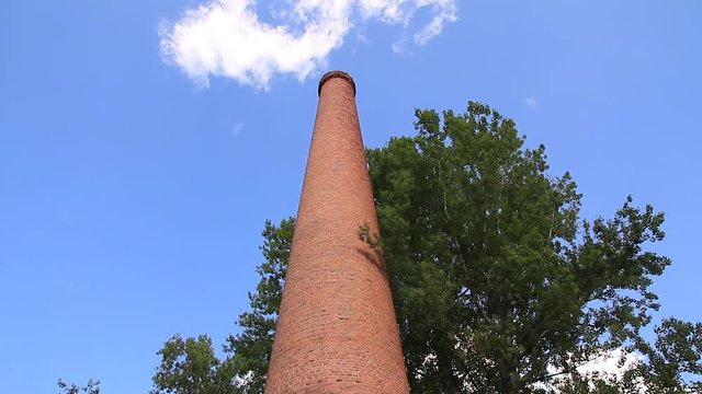 Antigua  chimenea industrial  construida  con ladrillos vista desde abajo y rodeada de arbolado verde 