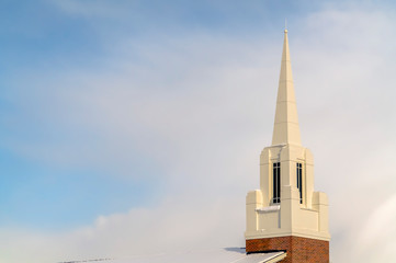 Snowy church steeple and roof against cloudy sky