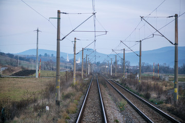 Eastern European railroad across Transilvania. Mountain landscape in the background. Scary, dangerous scene in winter with naked trees and polluted nature 