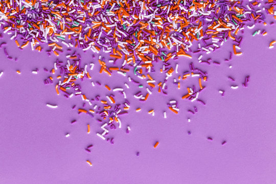 Colorful sprinkles on a purple background, top view with copy space