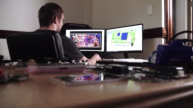 A mechanical engineer sits behind a 3D CAD workstation and monitors designing a high-tech electrical device.