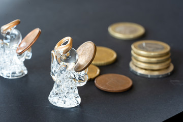 Glass angel figure over coins column on black background