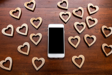 Smartphone on wooden table surrounded by wooden hearts. Saint Valentines day theme.