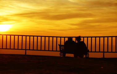 Sweet couple silhouette sitting on the mountain with sunset background