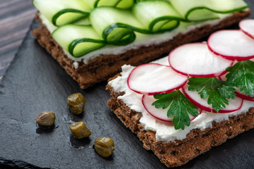 Toast with radish, cucumber and ricotta on a dark background. Healthy breakfast.