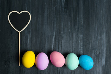 Obraz premium Multicolored eggs lie on a black wooden background, concept of a postcard for Easter