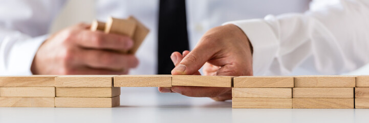Wide view image of businessman making a bridge of wooden pegs