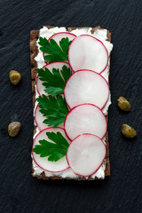 Snack with ricotta and radish on a black background, top view