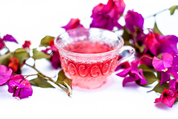 Close up shot of tea of Bougainvillea flowers in a  transparent glass cup isolated on white with raw flowers and leaves.