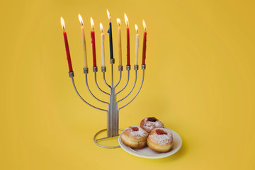 Hanukkah menorah and a plate of jelly doughnuts on a yellow background