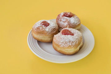 Three jelly doughnuts on a plate with yellow background - Hanukkah tradition