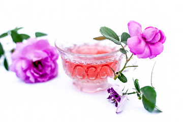Close up view of organic fresh rose tea in a transparent glass cup isolated on white with raw roses.