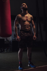 Shirtless tattooed athlete looking up by the heavy bag