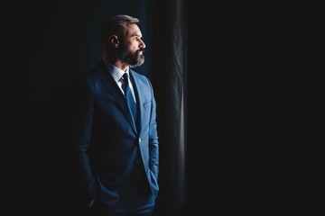 Thinking about... Thoughtful man in full suit looking away through the window while standing...