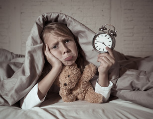 Little Girl in bed awake at night yawning and feeling restless showing clock she can not sleep
