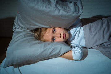 Little girl having trouble sleeping at night holding pillow covering her head and ears upset