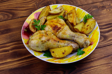 Baked chicken drumsticks with potatoes in a plate on wooden table