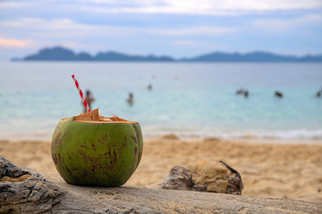 Green coconut drink with straw on sea beach sand. Coconut juice on tropical seashore. White sand beach relax.