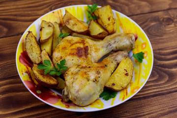 Baked chicken drumsticks with potatoes in a plate on wooden table