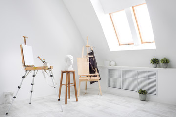 White and bright studio with a window. Workspace of the artist. Easel, canvases and plaster figures for learning to draw.