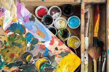 Paints of different colors and dirty brushes on the easel of the artist close-up.