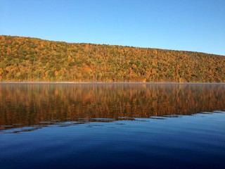The clear, still water of Canadice Lake, one of Finger Lakes in New York, in horizontal orientation in Autumn, with a blue sky background 