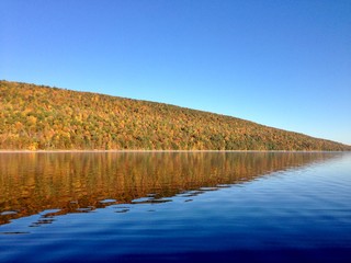 The clear, still water of Canadice Lake, one of Finger Lakes in New York, in horizontal orientation in Autumn, with a blue sky background 