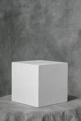 Gypsum white cube, simple geometric shape on a gray fabric art background for learning to draw.