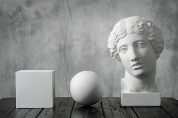 Gypsum white cube, sphere and head of an antique woman simple geometric shape on a gray fabric art background for learning to draw.