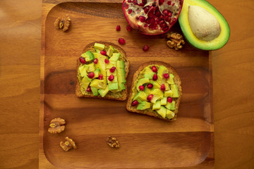 Two Avocado Toasts with pomegranate seeds on a wooden tray