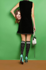 Full length back shot of lady wearing a sleeveless dress and striped high knee socks, holding her...