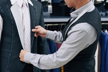 Cropped image of tailor fitting bespoke suit to client in atelier