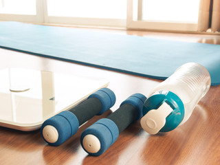 Fitness equipment and health care concept form Weight Scale, dumbbells, mat yoga, handkerchief and drinking water, Flat lay on wooden floor of apartment for in home workout.