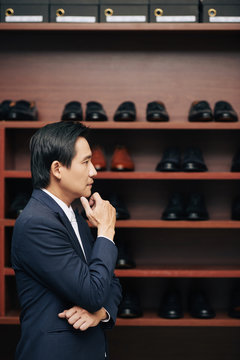 Pensive mature man standing at shoe shelf in fashion boutique