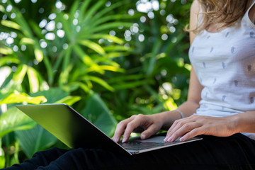 Girl using her laptop in garden workplace, typing on device. Young woman using laptop computer. Female working on laptop in an outdoor garden. Businesswoman working and studying, online contents.