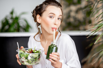 Beautiful woman drinking smoothie while sitting with healthy salad in the bathroom. Healthy eating...