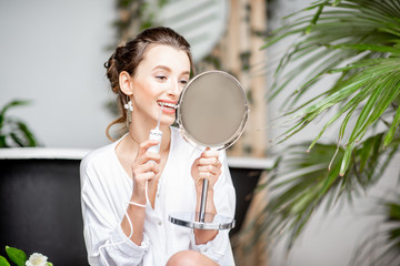 Beautiful woman cleaning teeth with irrigator tool looking into the mirror in the bathroom