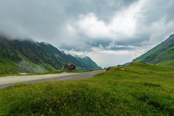 transfagarasan road in stormy weather. popular travel destination of romania. grassy meadow along...