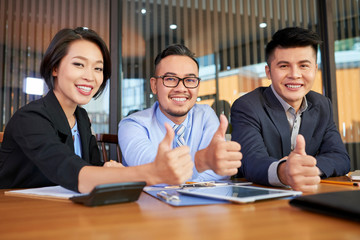 Team of happy Asian entrepreneurs showing thumbs-up to express approval