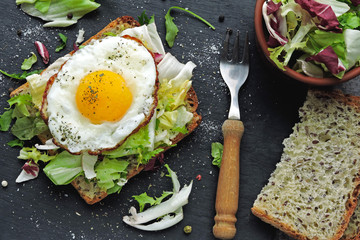Bran toast with salad mix and fried egg on top. Healthy breakfast presented on a stone board. Keto diet. Keto breakfast or snack.