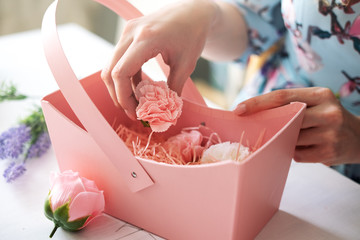 Florist collects a bouquet of pink rose buds and carnations in a pink paper basket.